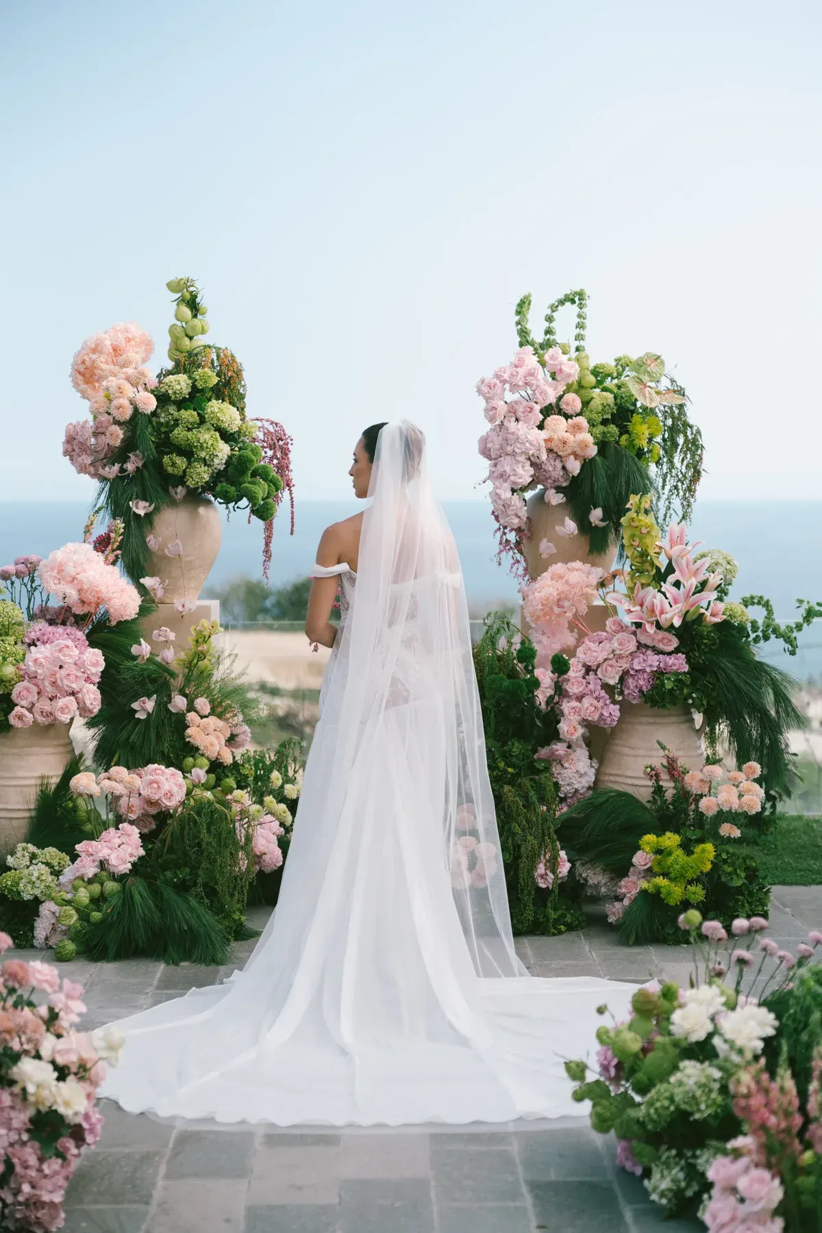 A bride in her veil, facing the ocean before the ceremony