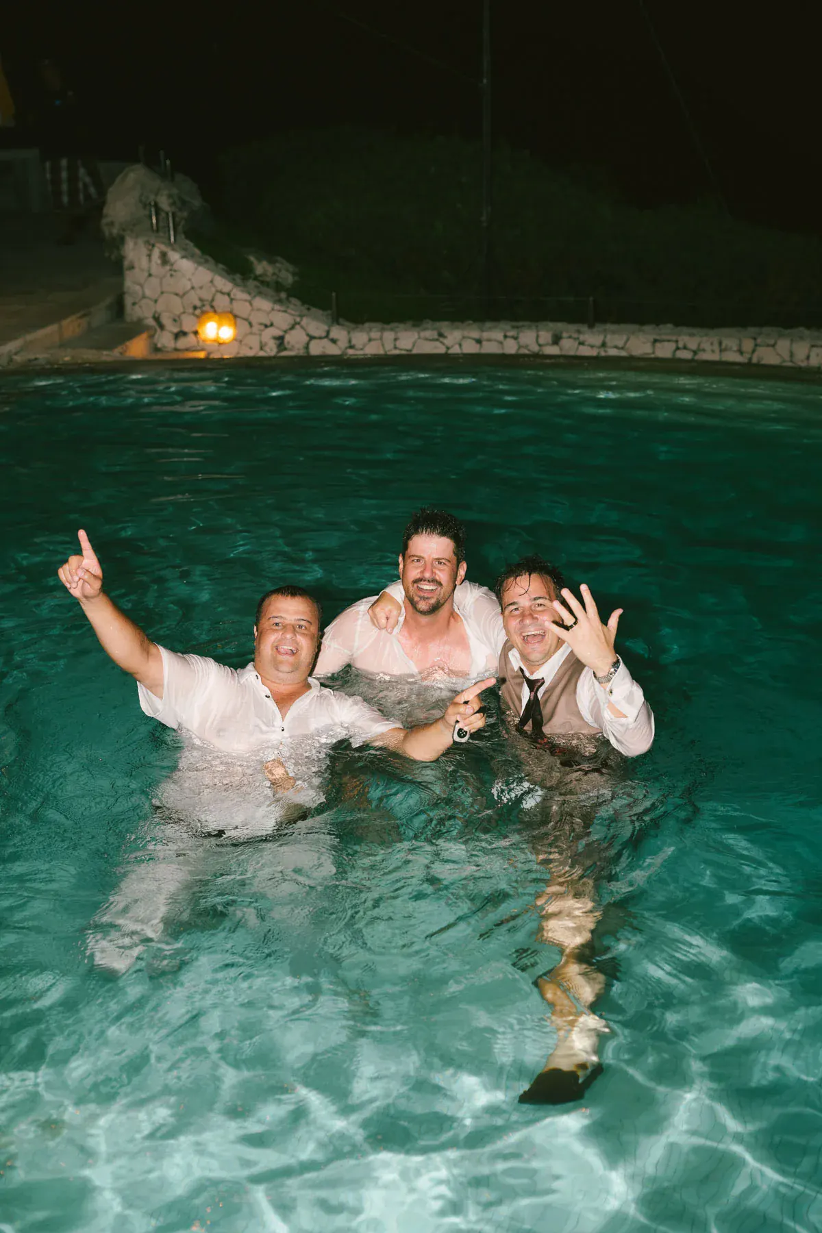Groomsmen celebrating at the infinity pool after dark